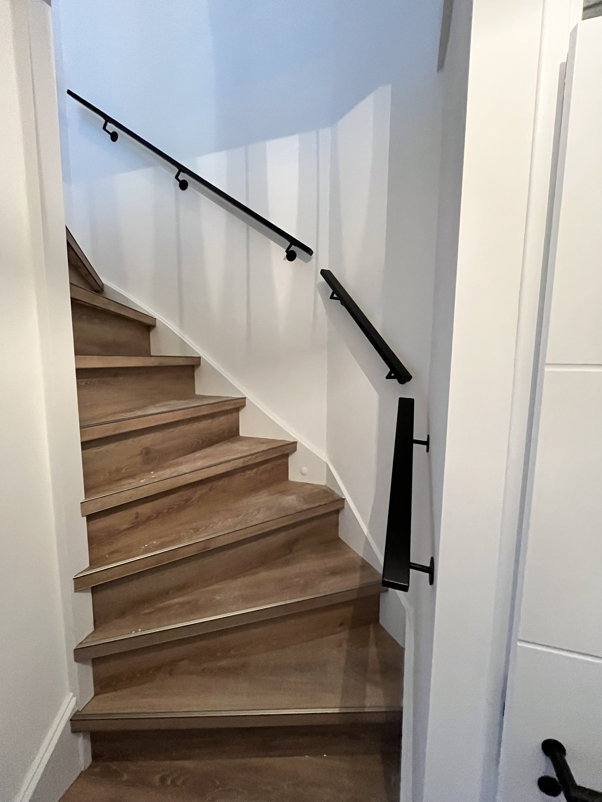 Een vernieuwde trap met eikenkleurige treden en een zwarte leuning langs een witte wand