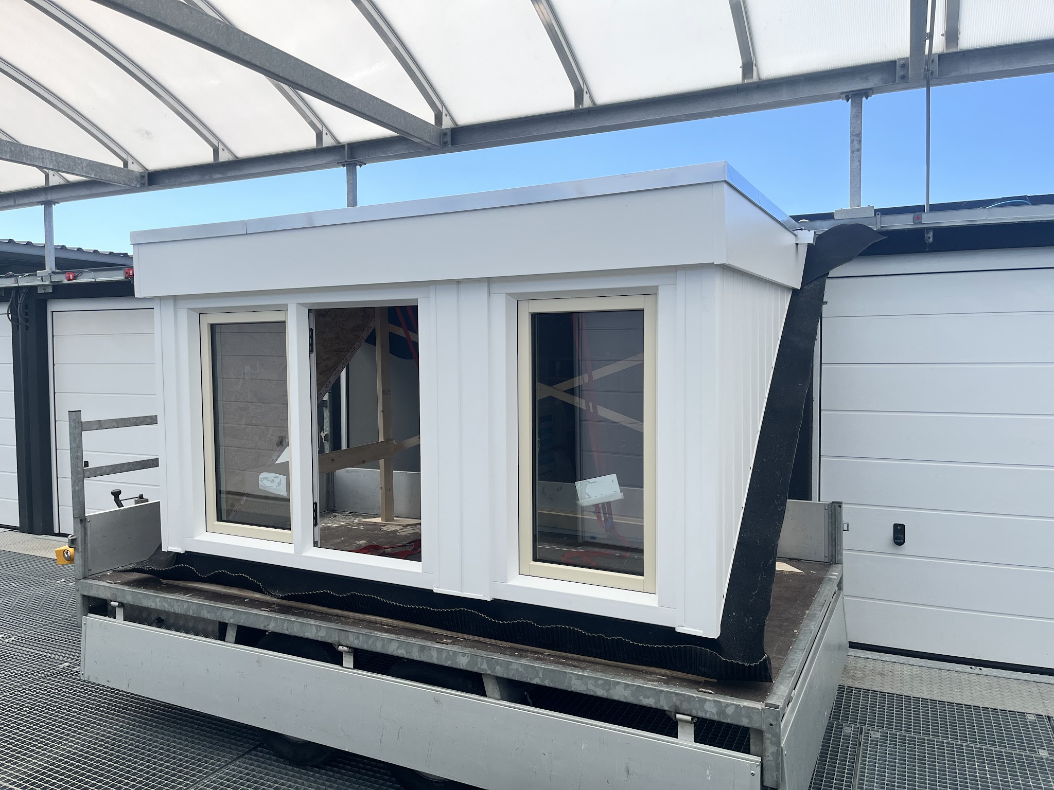 Een witte prefab dakkapel met drie ramen op een aanhanger in een hal