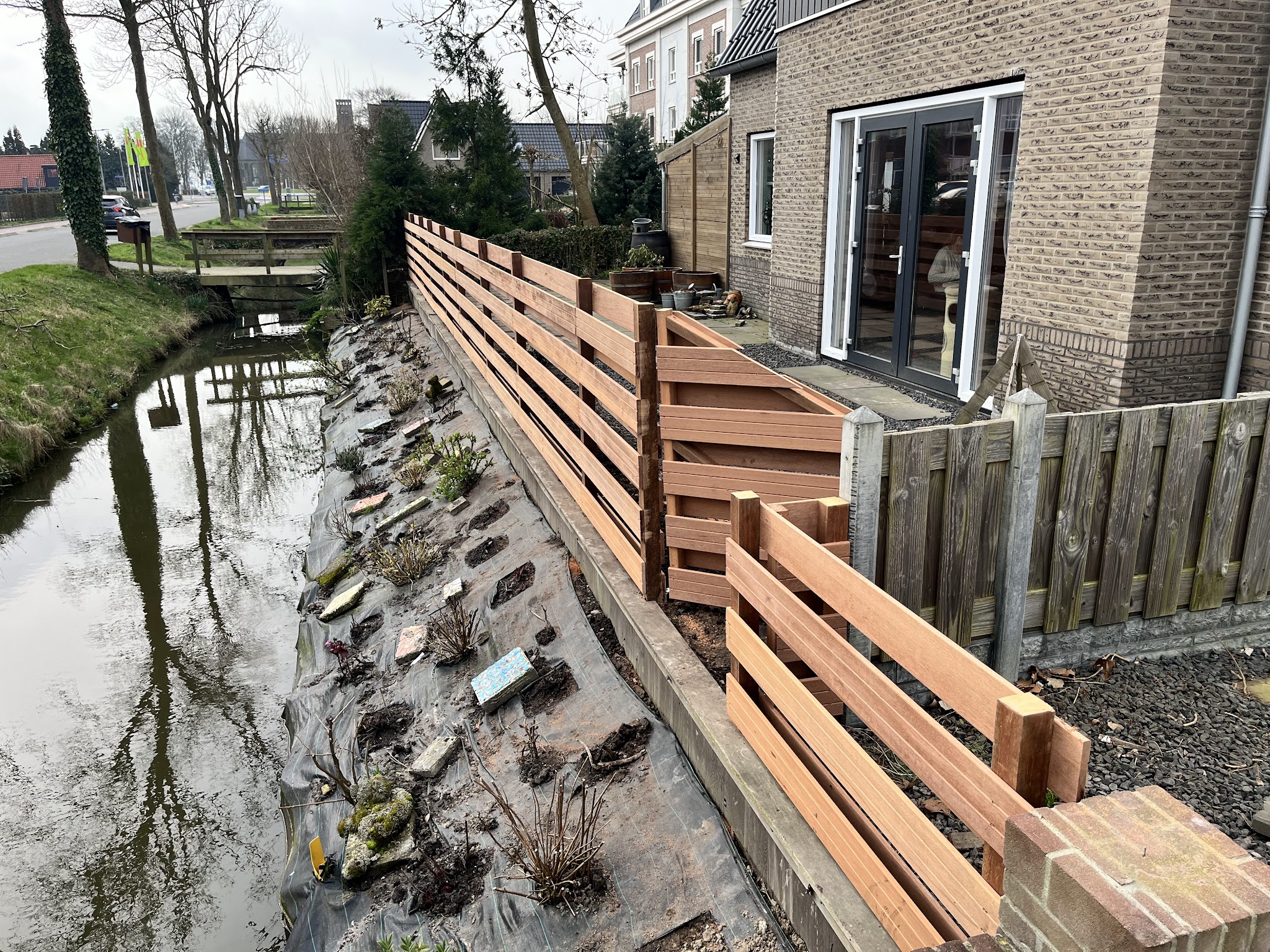 Een nieuwe houten schutting en beschoeiing langs een sloot naast een woning