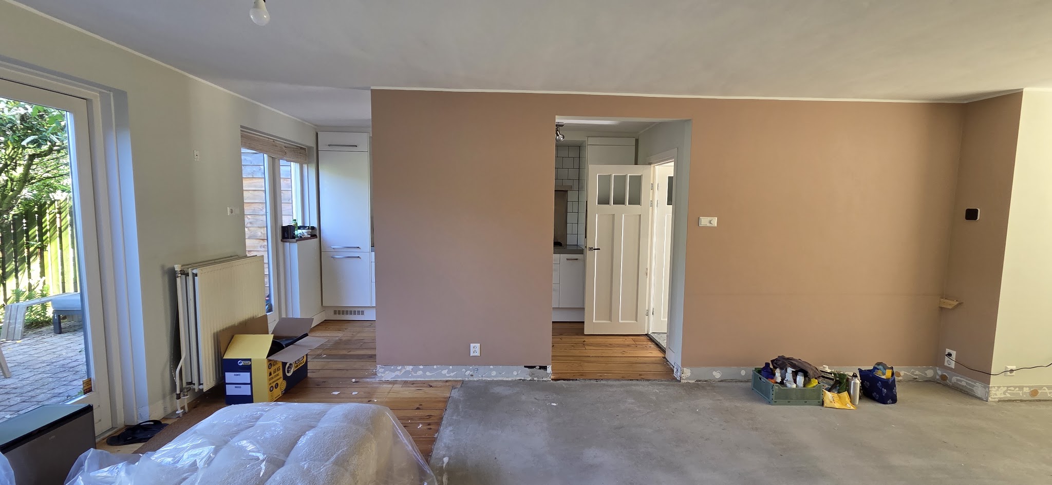 Een woonkamer tijdens de verbouwing, met een doorgebroken wand en de vloer die gelegd wordt